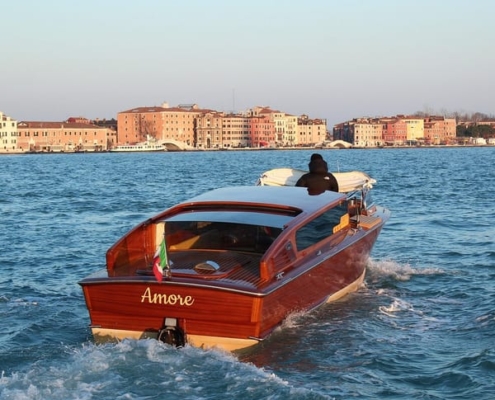 A luxury wooden motorboat cruising past grand Gothic and Baroque palaces on the Grand Canal in Venice, Italy